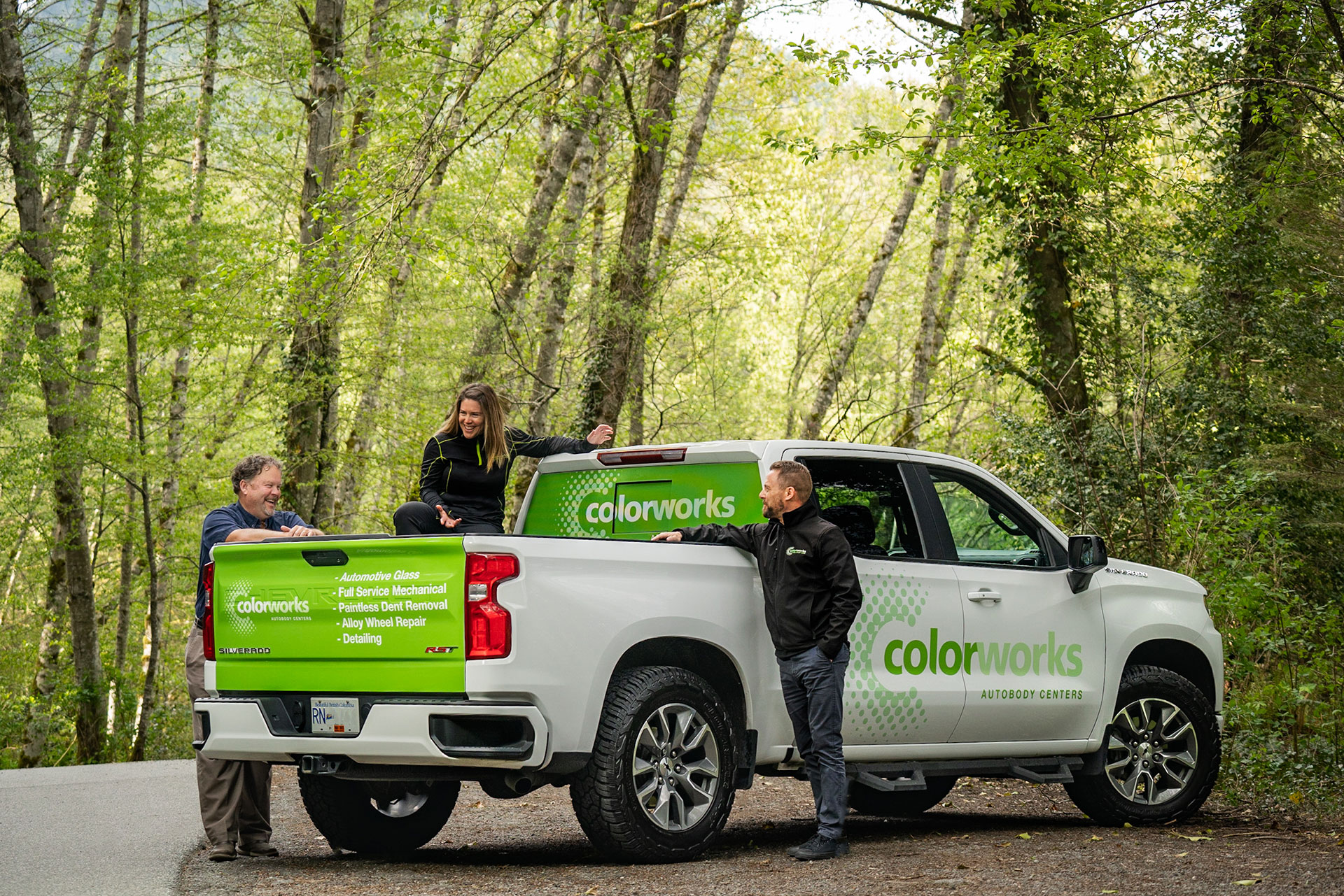 Friendly Colorworks staff with branded truck in forest background.