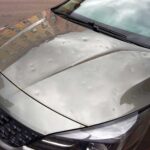 Vehicle showing multiple hail-impact dents on its body panels after a hailstorm.