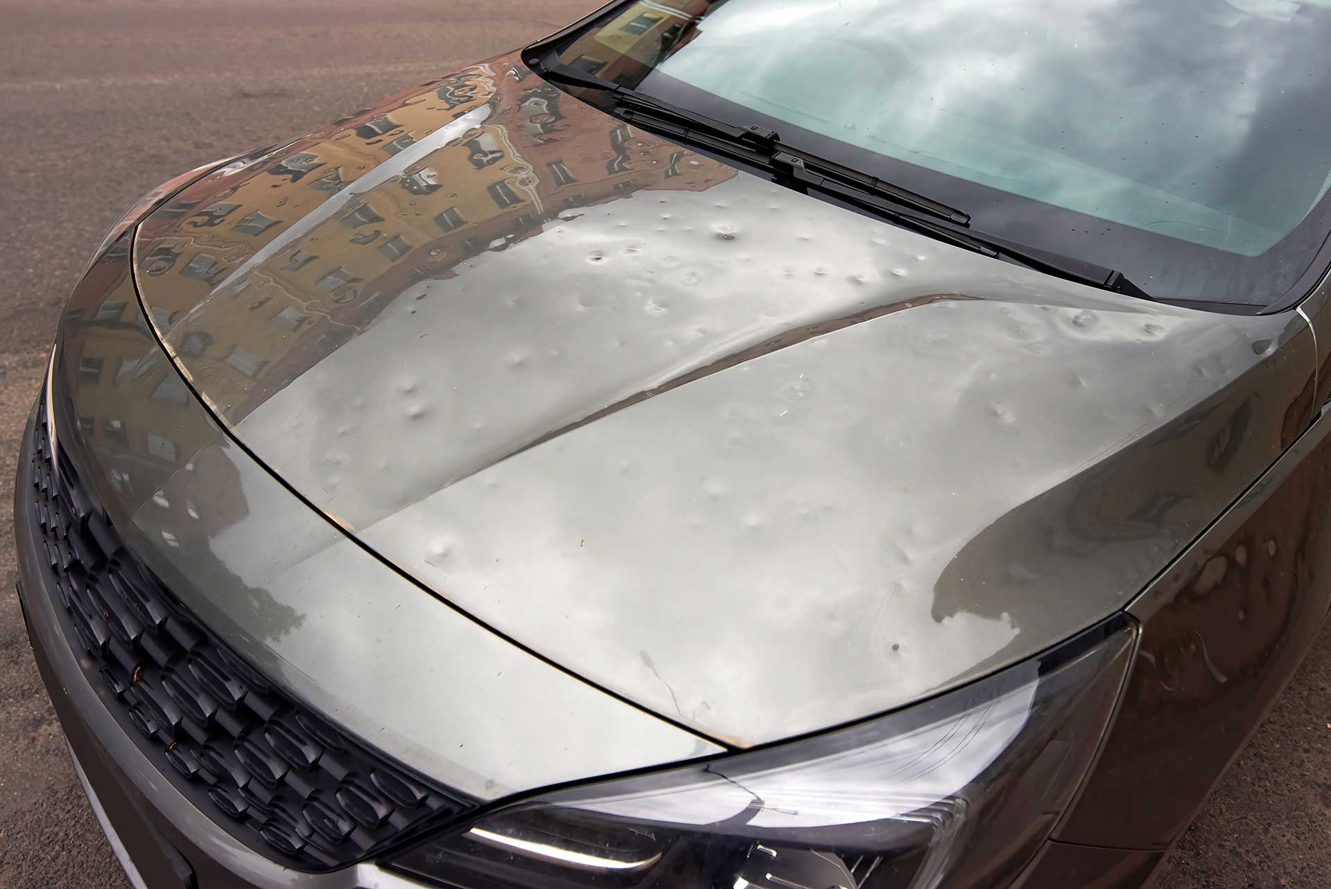 Vehicle showing multiple hail-impact dents on its body panels after a hailstorm.