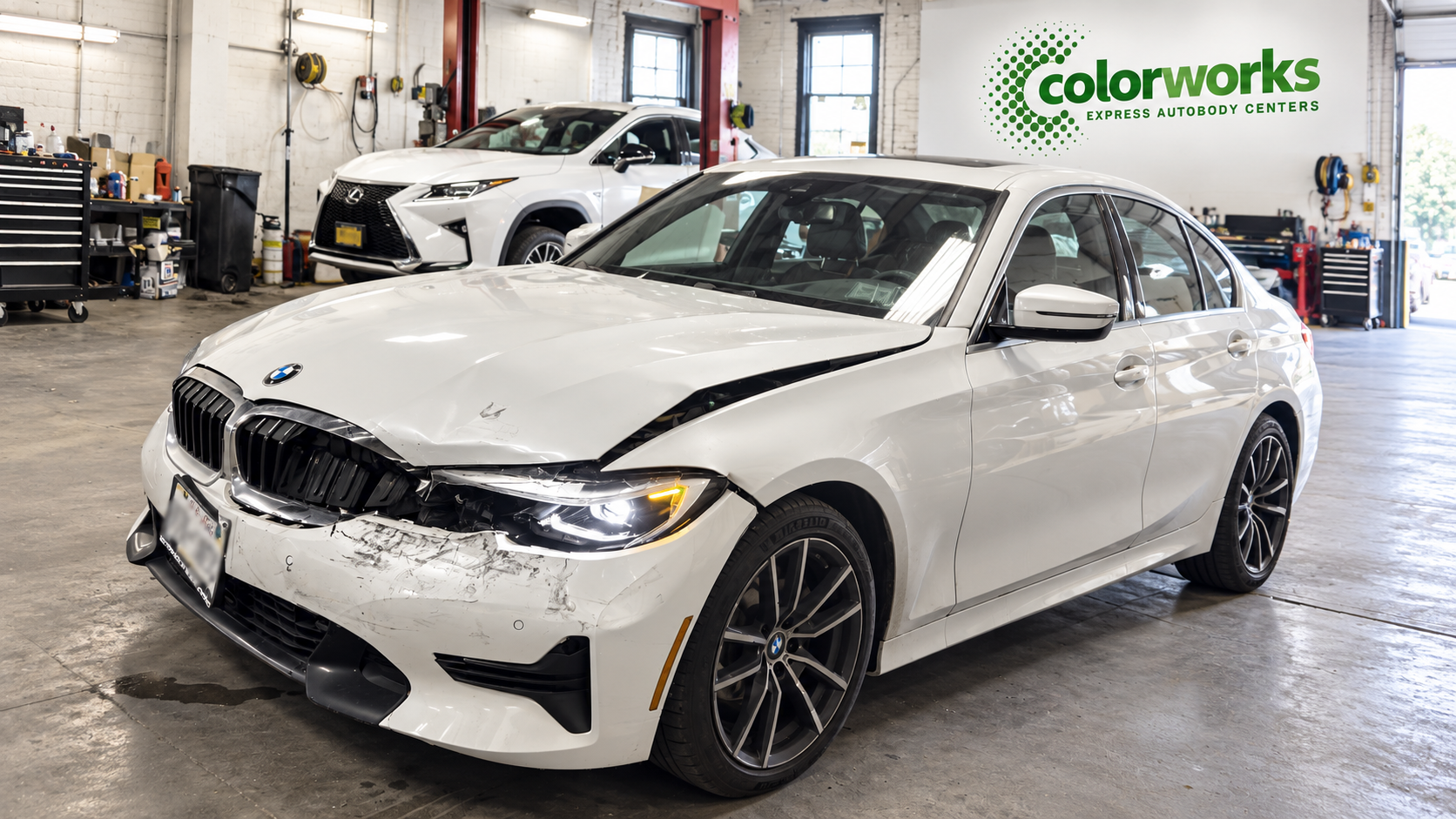 Damaged white BMW sedan in a repair workshop with Colorworks Express branding