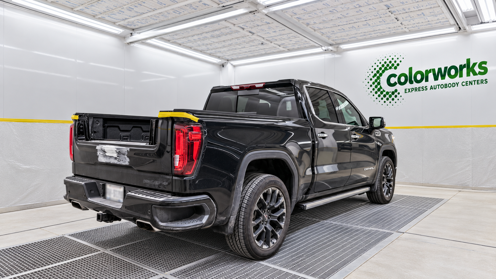 Black GMC Sierra pickup undergoing body repairs in a paint booth, with Colorworks Express branding