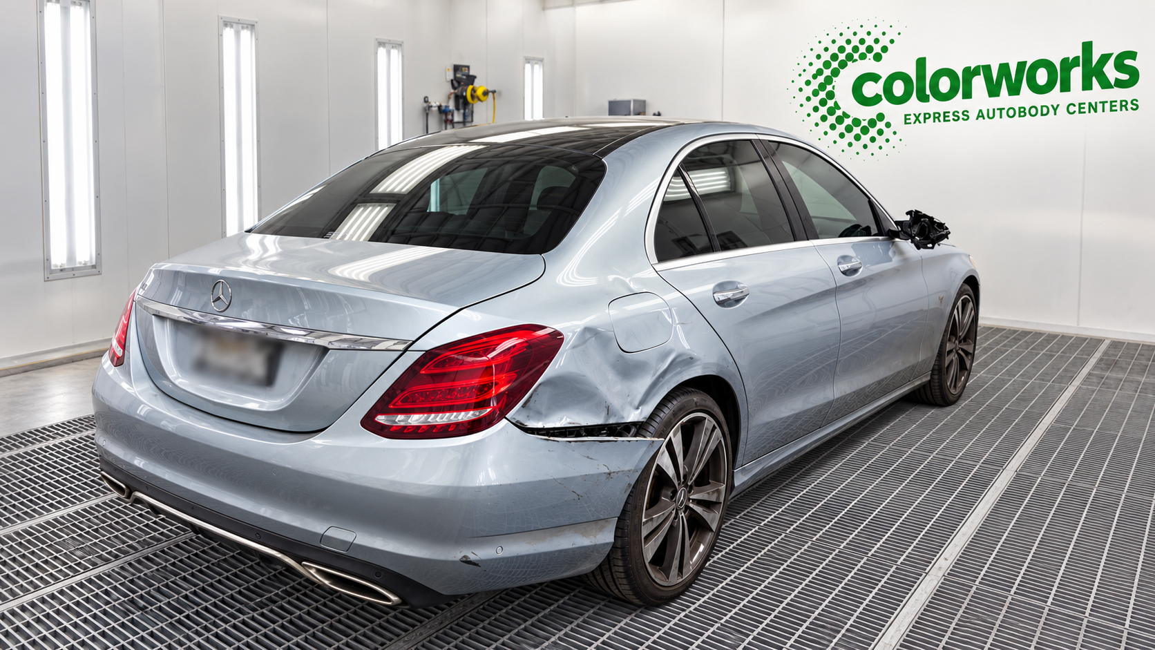 Silver Mercedes-Benz sedan with collision damage in a paint booth, with Colorworks Express branding